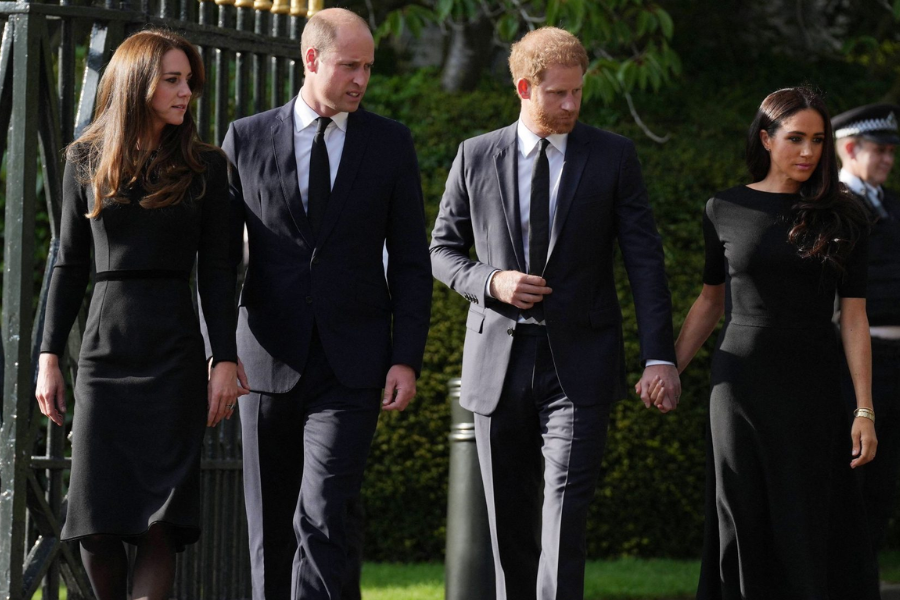 Four individuals walk together outdoors dressed in black formal attire, likely for a mourning or memorial event. The two women wear knee- to floor-length black dresses, while the men are in dark suits and ties. One couple walks hand in hand, while the other walks side by side.