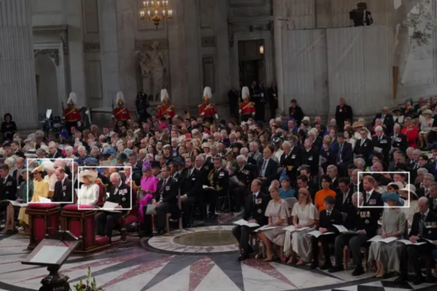 A wide-angle view of a formal ceremony inside a grand hall, with rows of seated attendees dressed in formal attire. Members of the royal family are boxed for emphasis, seated in separate sections. The scene includes ornate architecture, uniformed guards, and a central marble floor with a decorative pattern.