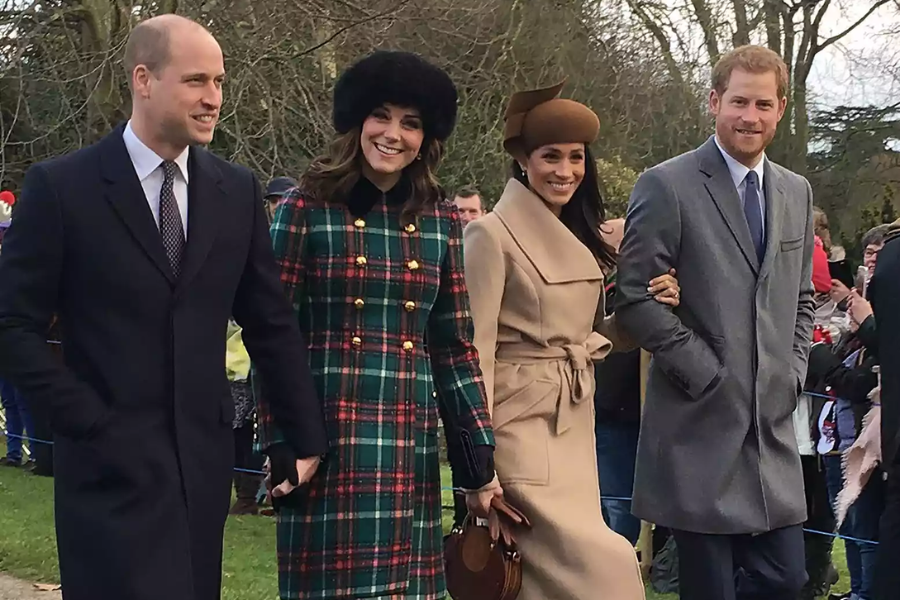 Two couples walk side by side outdoors, dressed in winter coats for a formal holiday event. The man on the left wears a dark coat, next to a woman in a green and red plaid coat with gold buttons and a black fur hat; beside them, a woman in a camel coat with a matching brown hat holds onto a man in a gray coat with his hands in his pockets.