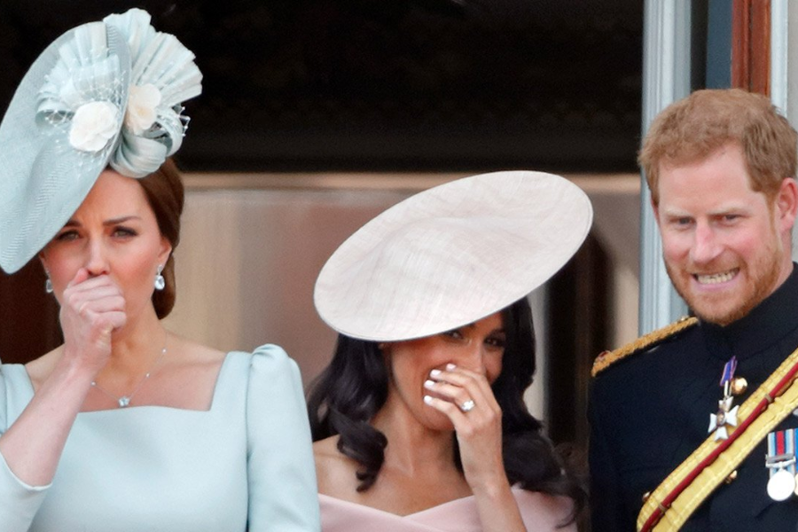 Three individuals stand on a balcony during a formal royal event, caught in a candid moment. The woman on the left in a pale blue dress and matching fascinator covers her mouth as if stifling a laugh or cough. The woman in the center, wearing a blush pink dress and wide-brimmed hat, also covers her mouth while smiling. The man on the right, dressed in military uniform, smiles tensely.