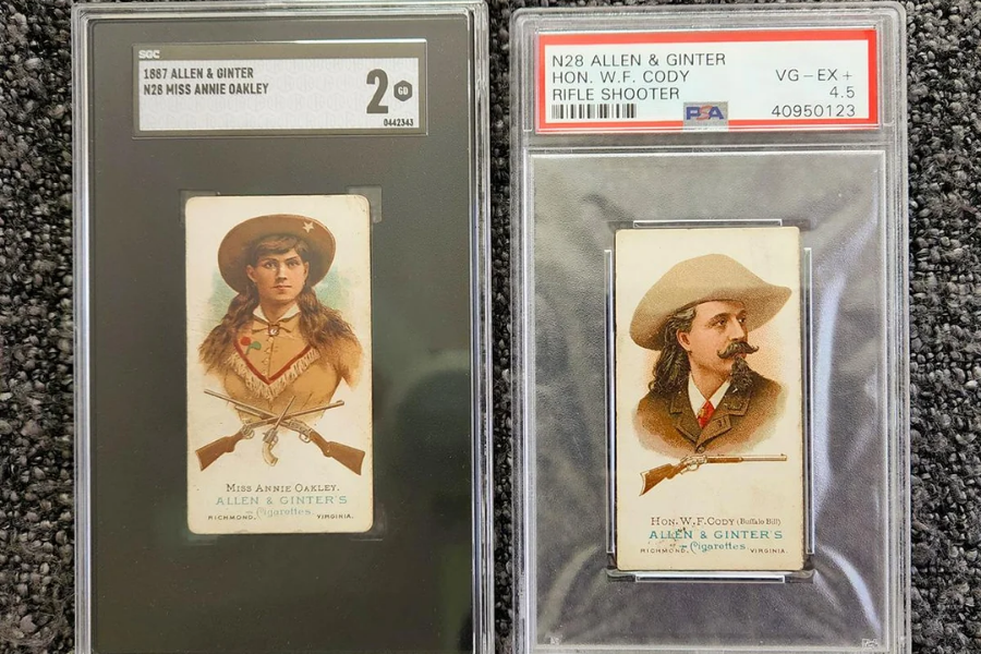 Two vintage Allen & Ginter trading cards displayed in protective cases: the left card features Miss Annie Oakley in a fringed outfit with crossed pistols and rifles beneath her portrait; the right card features Hon. W. F. Cody (Buffalo Bill) in a brown suit with a long mustache and a rifle illustration below. Both cards are graded and labeled with their respective names and ratings.