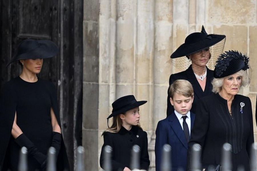 A solemn group of individuals dressed in formal black mourning attire stands outside a stone building during a ceremonial event. The women wear veiled hats and gloves, while two children, a young girl and boy, stand between them in matching dark outfits, looking down or to the side respectfully.