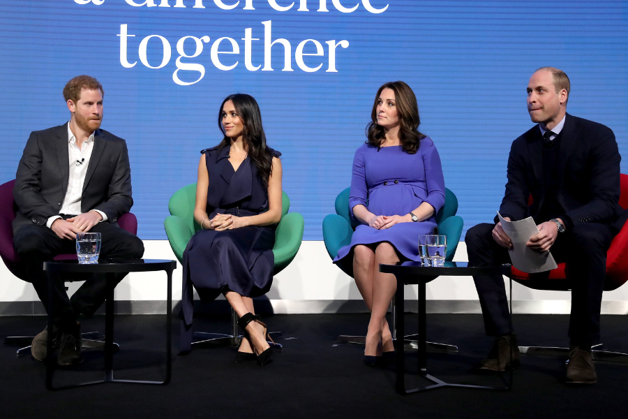 Four individuals sit on stage in colorful chairs during a panel discussion, with the words “a difference together” displayed behind them. From left to right: a man in a dark suit with an open-collared shirt, a woman in a sleeveless navy dress, a woman in a bright purple dress cradling her baby bump, and a man in a suit holding papers.