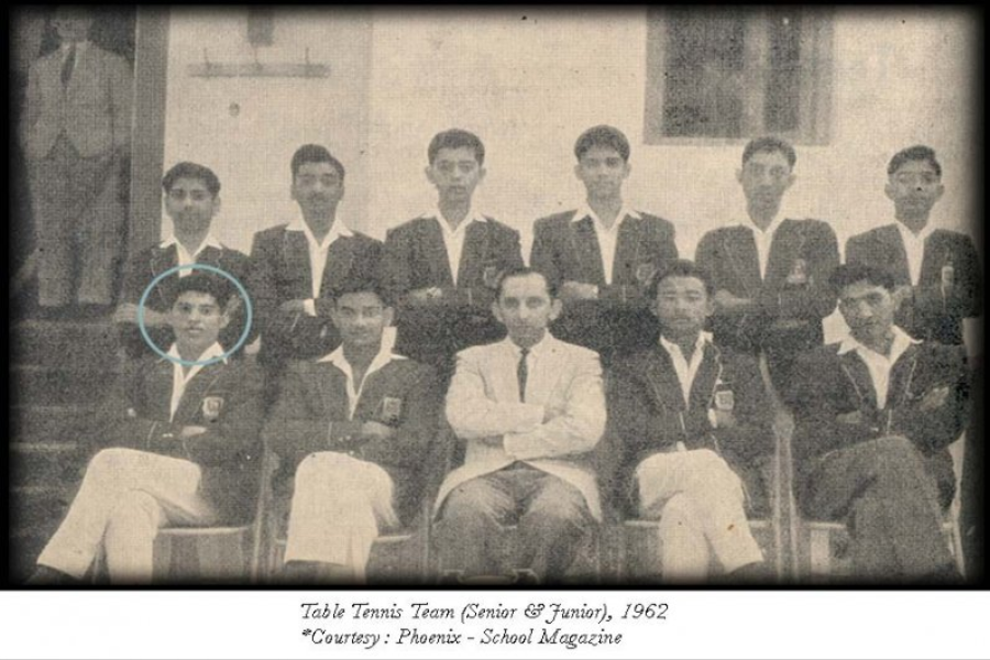 Black-and-white group photo of the 1962 Table Tennis Team (Senior & Junior) posed on steps, with most members in dark blazers and white trousers. A young male student seated in front on the far left is circled, possibly to highlight his identity. The team is accompanied by a man in a light-colored suit at the center, likely the coach or faculty member.