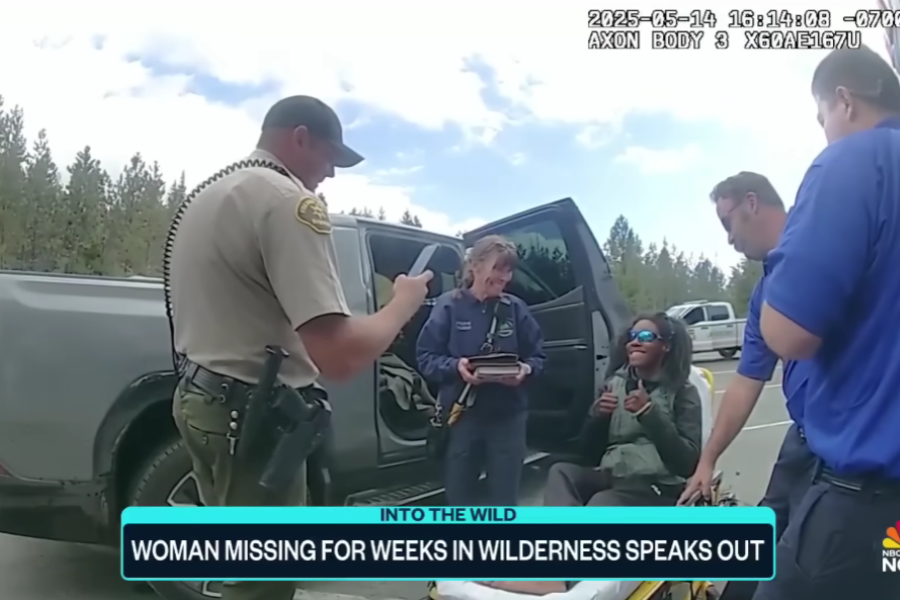 woman wearing sunglasses gives a thumbs-up while seated on a stretcher, surrounded by law enforcement and emergency personnel next to a parked vehicle. The scene is outdoors with trees in the background, and the image is overlaid with a news banner that reads: "INTO THE WILD — WOMAN MISSING FOR WEEKS IN WILDERNESS SPEAKS OUT."
