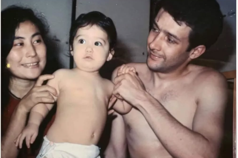 Color photograph of a smiling woman and a shirtless man holding a baby between them. The baby, wearing only a diaper, looks off to the side with a curious expression while both adults gaze at the child fondly.